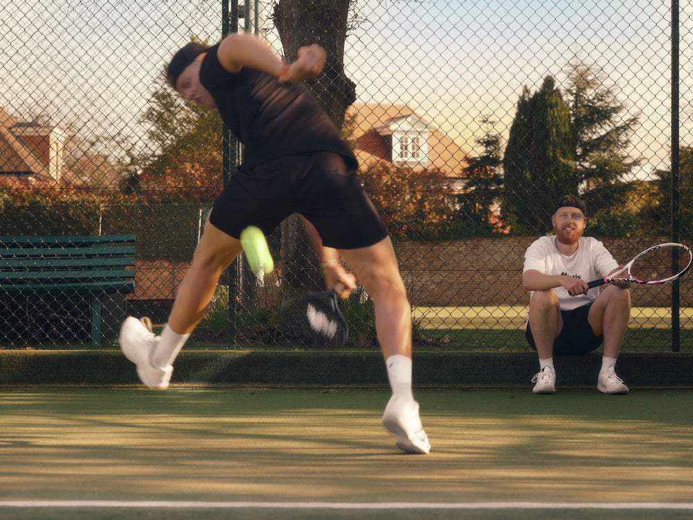 tennis player hitting powerful shot on court with coach watching holding racket behind fence