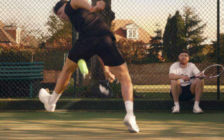 tennis player hitting powerful shot on outdoor court with coach watching holding tennis racket