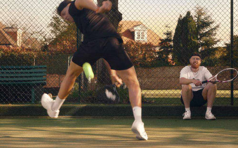 tennis player hitting powerful shot on court with coach watching holding racket behind fence