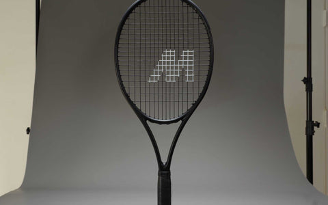 black tennis racket with M logo on strings in professional stringing studio with softbox lighting